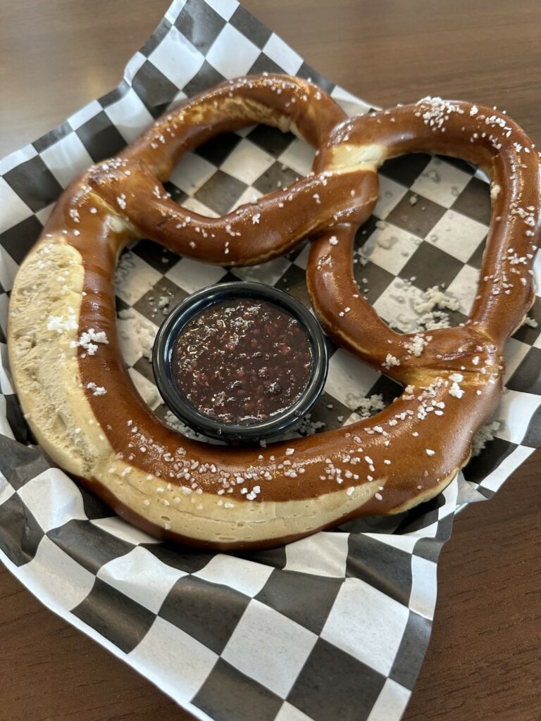 Salted pretzel with dipping sauce on checkered paper.